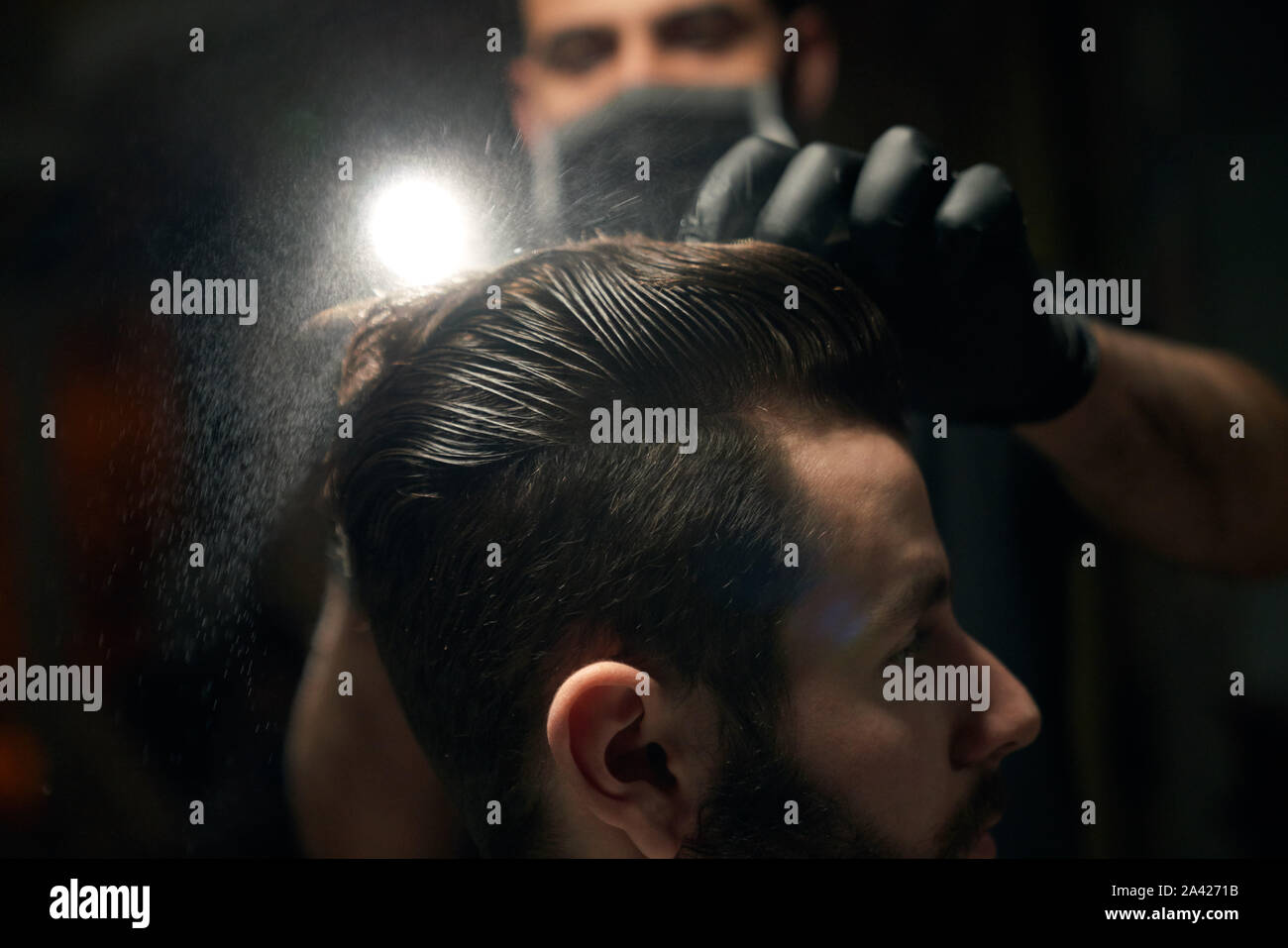 Close up of brunette man s head with clean wet hair that is combing by masculine hairdresser in black gloves.Young bearded male in barbershop changing his haircut to be more trendy and stylish Stock Photo
