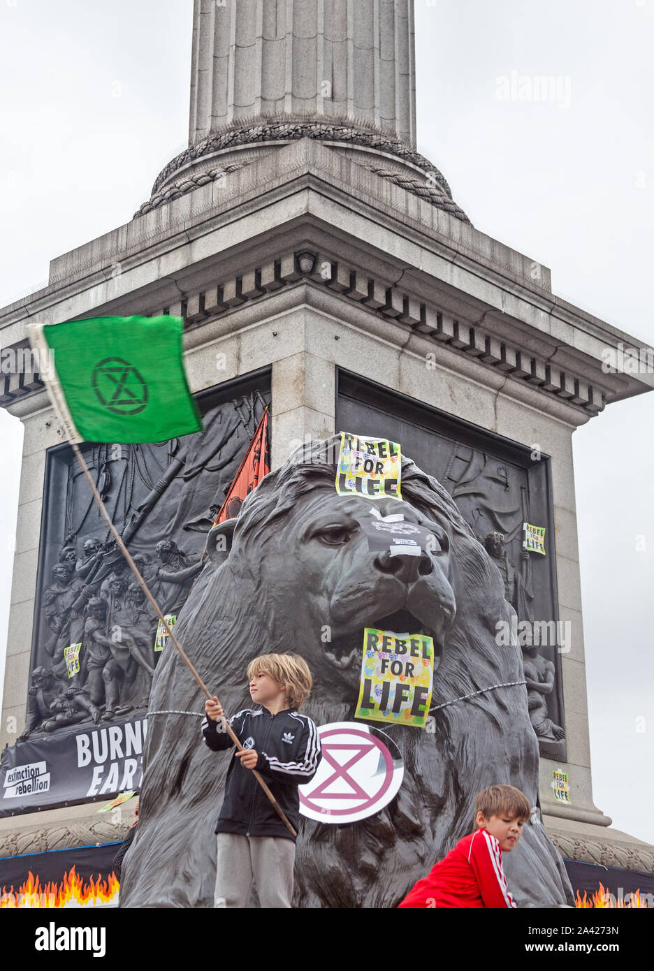October 8th, 2019. The first day of Extinction Rebellion's occupation of Trafalgar Square. Young demonstrators  on a  lion plinth waving XR flag. Stock Photo