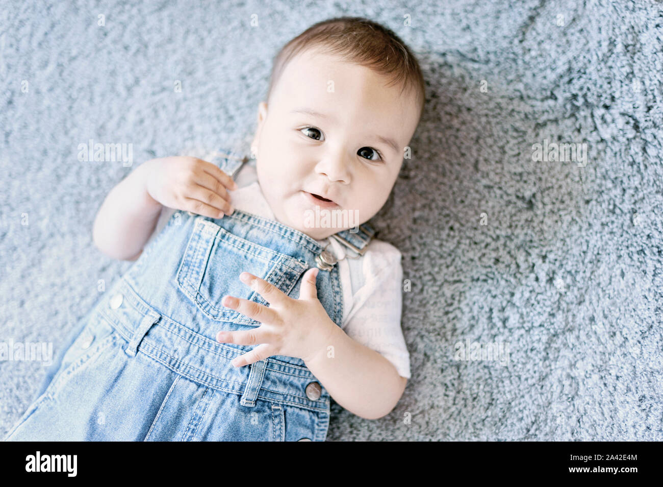 Funny little baby boy in denim lying on grey blanket. 6 month old child