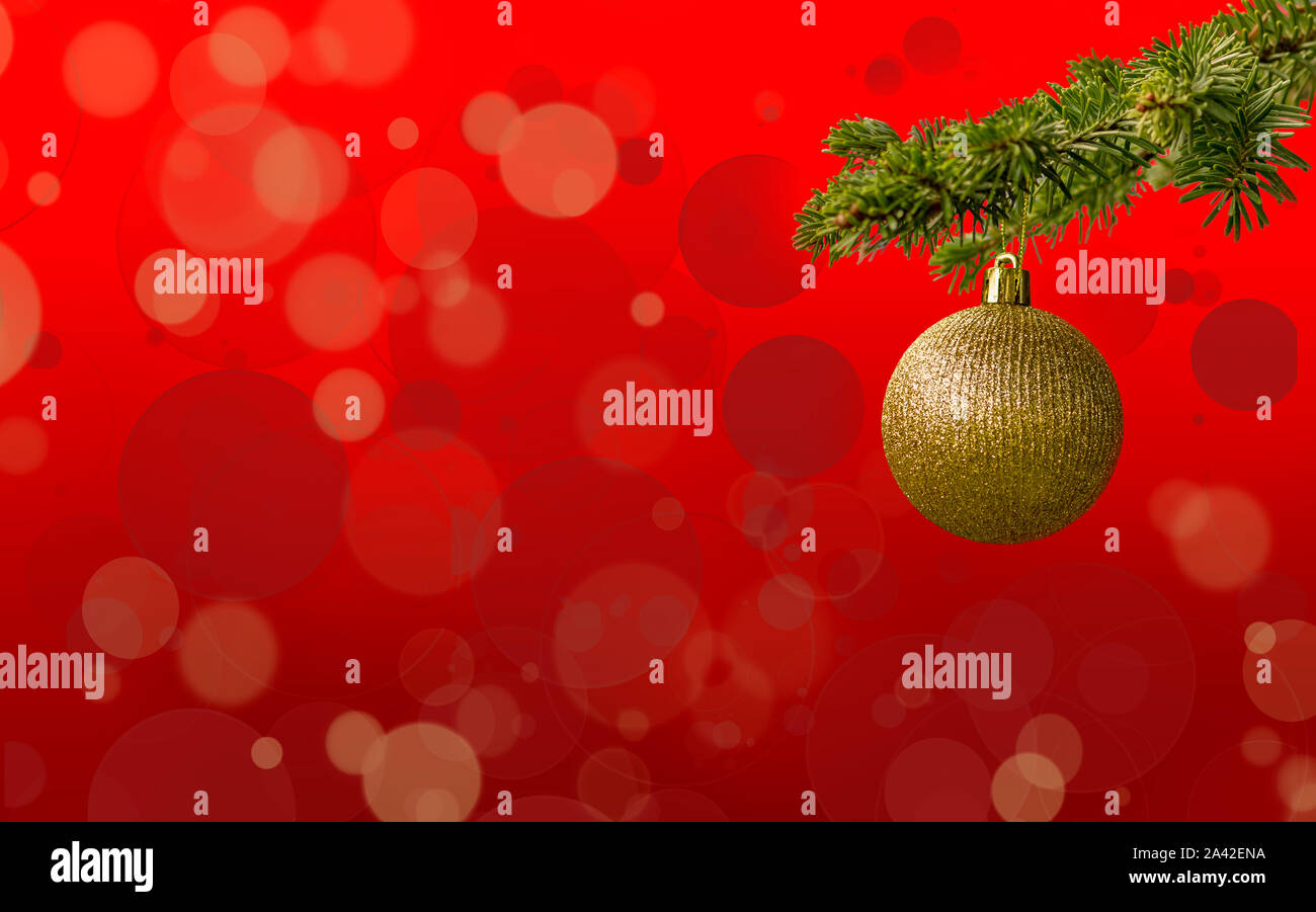 Fir tree branch with a golden glitter ball on red background. Bokeh effects. Christmastime. Christmas postcard. Stock Photo