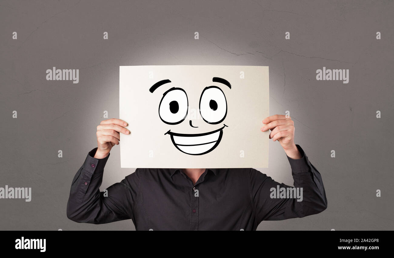 Young student holding a paper with laughing emoticon in front of his ...
