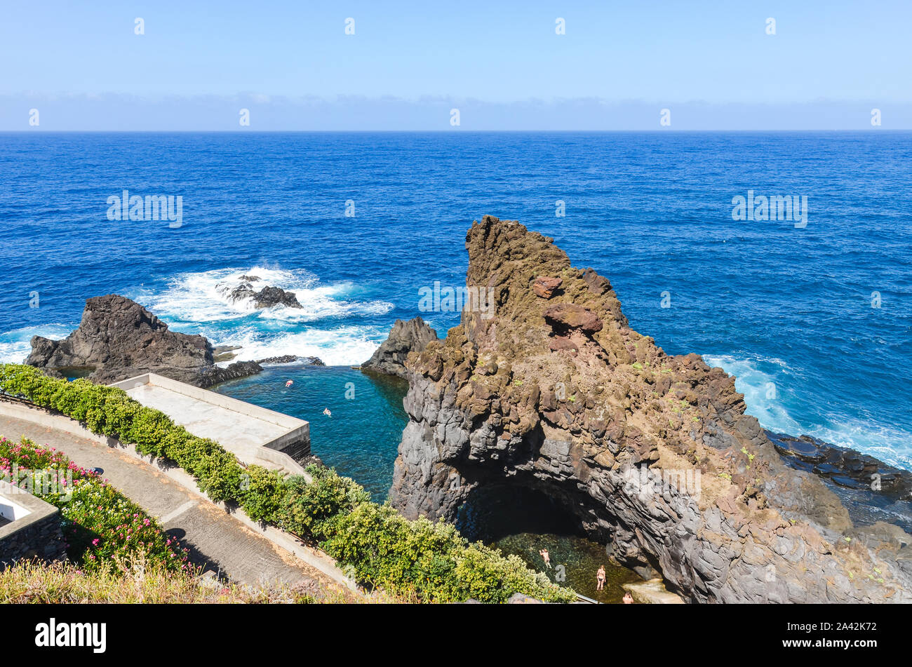 People swimming in natural swimming pools in the Atlantic ocean in Seixal, Madeira island, Portugal. Pool surrounded by volcanic rocks from open sea. View from above. Summer vacation spot. Stock Photo