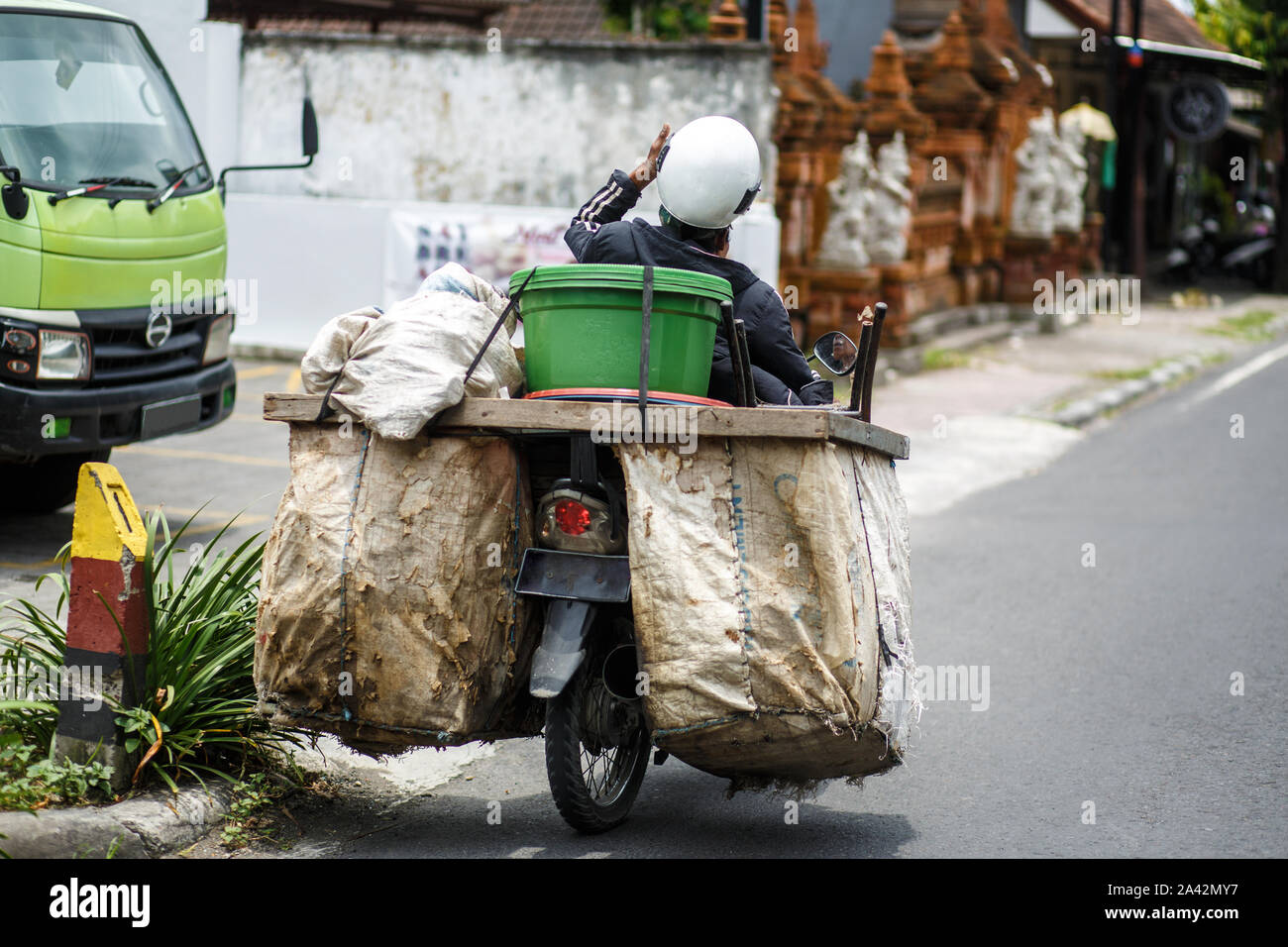 Asian biker trader rides a motorcycle on a road to which huge bags of groceries are tied Stock Photo
