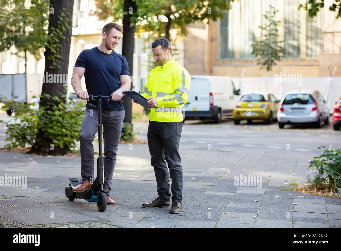 Officer Holding Clipboard In Hand Standing With Man Riding Electric Scooter On City Street Stock Photo