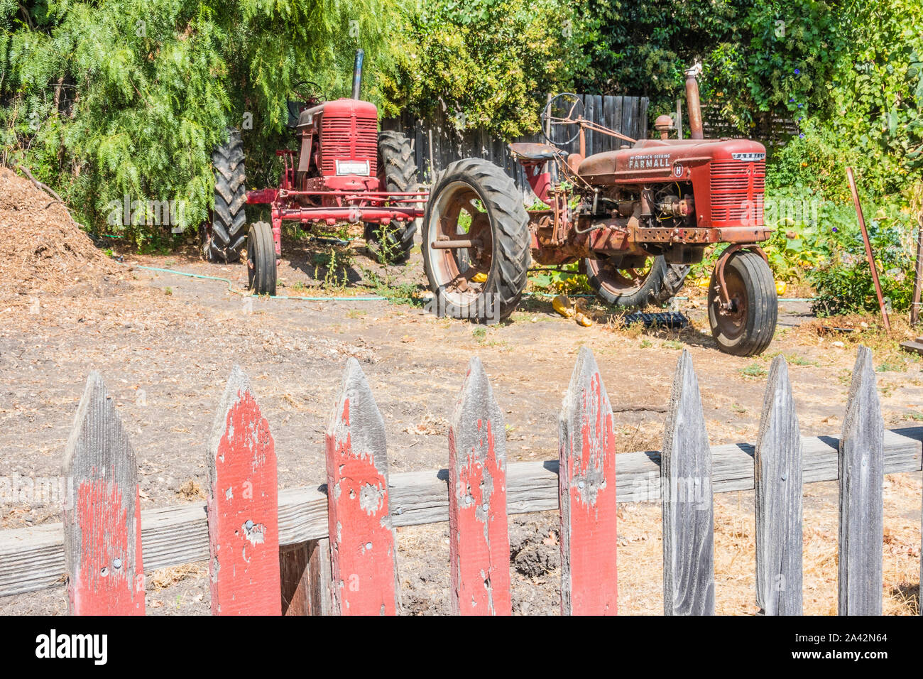 Two old red tractors parked with a weathered red wooden picket fence in the foreground in Los Olivos, California. Stock Photo