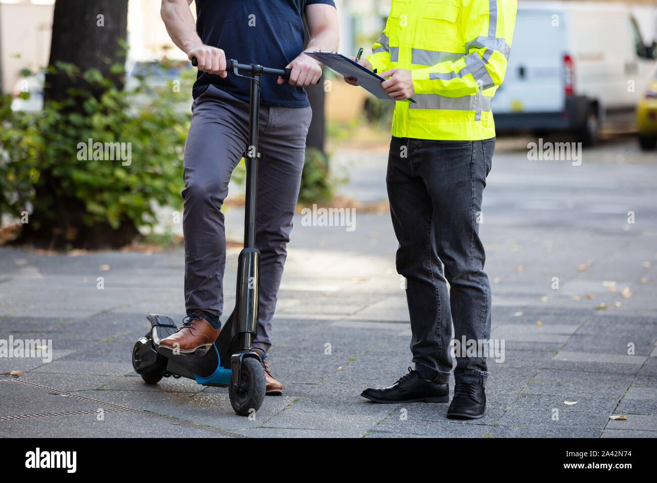 Officer Holding Clipboard In Hand Standing With Man Riding Electric Scooter On City Street Stock Photo