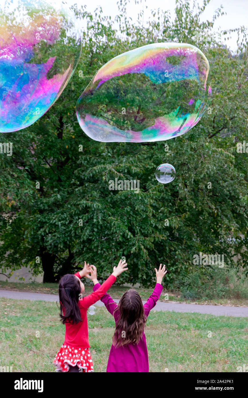 Two young girls reaching and trying to catch giant bubbles. Stock Photo