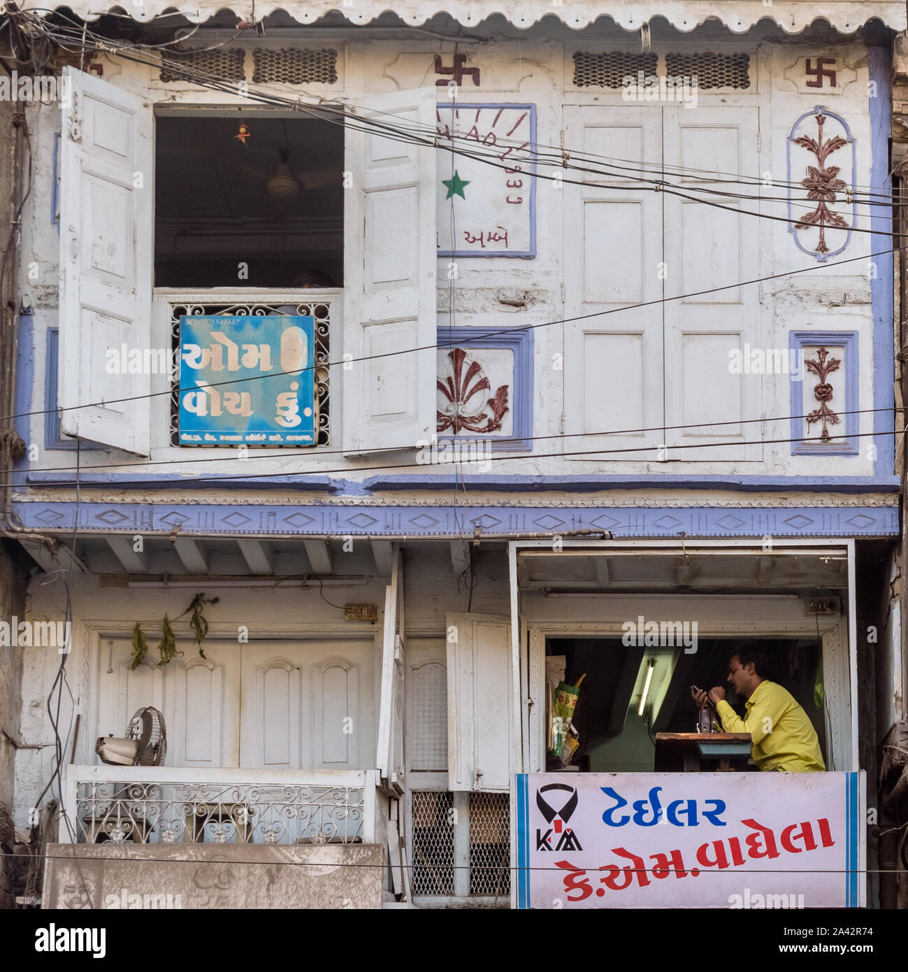 The quaint decorated windows of an old wooden building in the Bhavnagar market,  one of whom houses the shop of a tailor, has Gujarati signage. Stock Photo