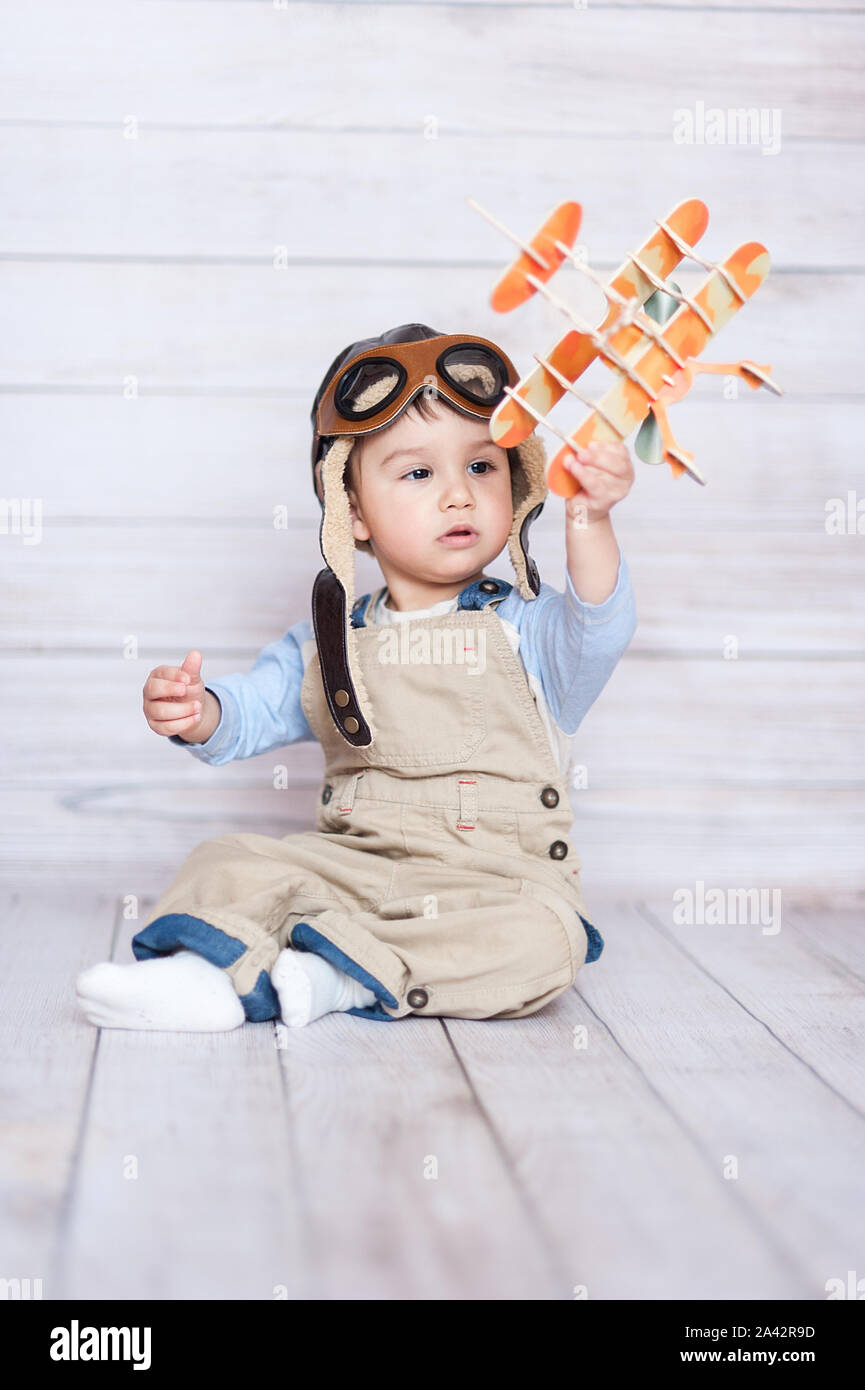 cute smiling baby in the cap of the pilot and wooden model of airplain