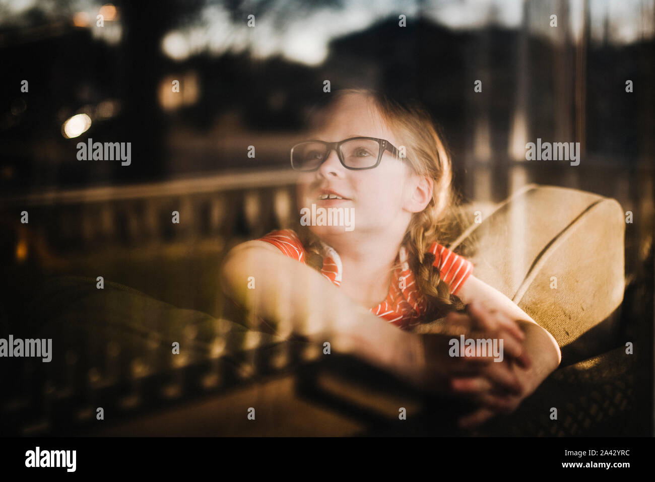 Front view of little girl looking out of window with reflections Stock Photo