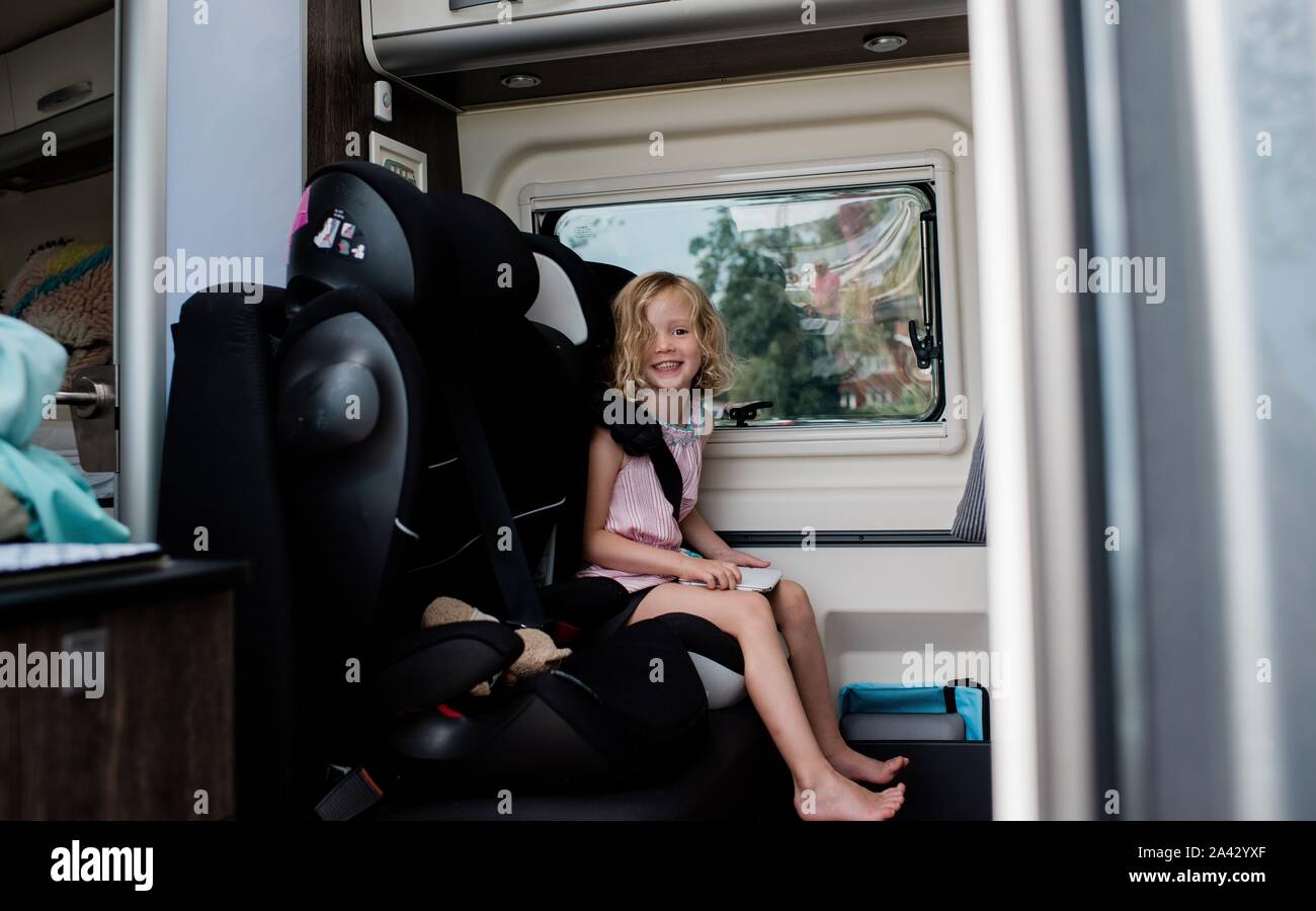 young girl sitting in a car seat in a camper van smiling holding ipad Stock Photo