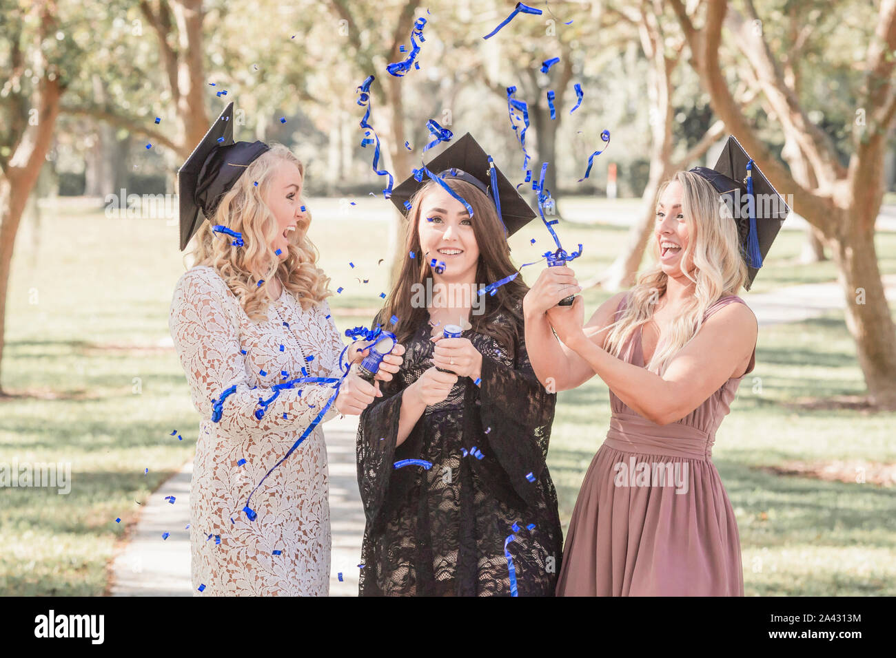 Three caucasian women in graduation caps laughing and popping confetti Stock Photo