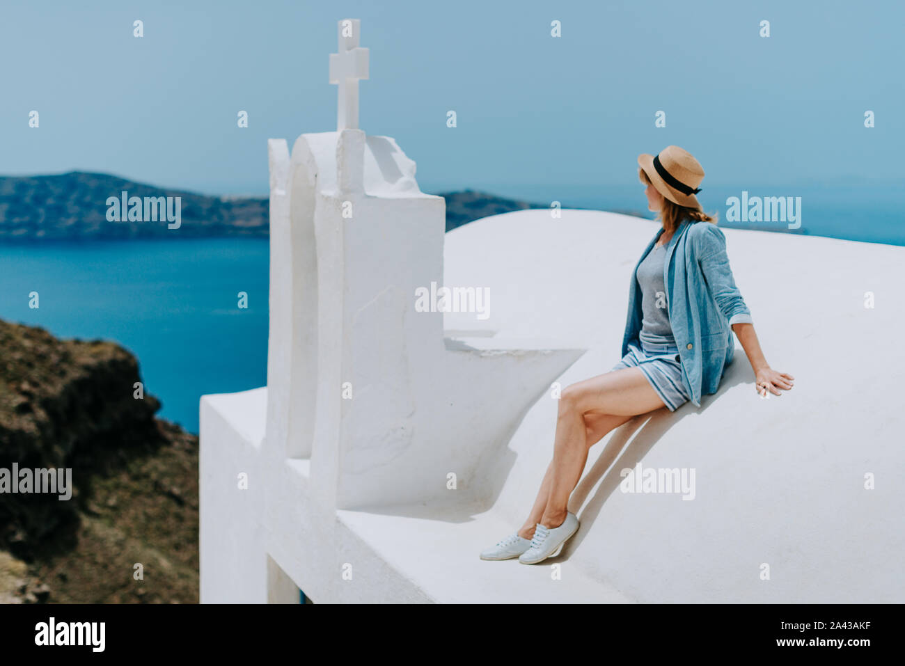 Santorini travel tourist woman on vacation in Oia walking. Girl visiting the famous white village with the mediterranean sea and blue domes. Europe summer destination. Beautiful Girl on the Roof of the White Church on the background of the Island of Santorini Stock Photo