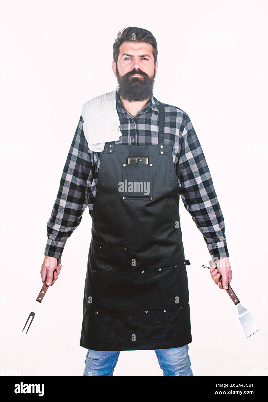 Being ready for bbq party. Grill cook holding spatula and bbq fork. Bearded man with bbq tools in hands. Happy hipster using stainless steel tools for preparing bbq food. Stock Photo