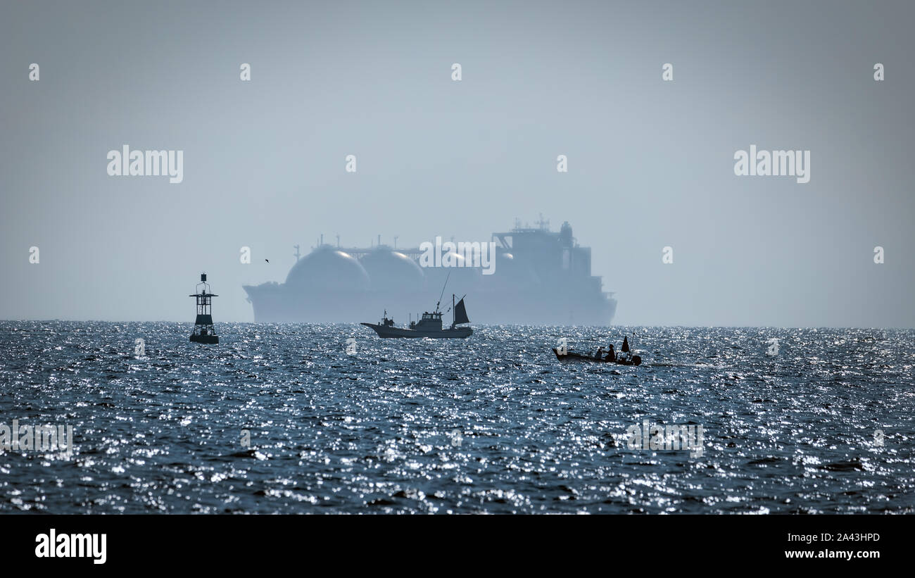 Two fishing boats being over shadowed by a Liquid Natural Gas tanker (LNG) in Japan’s Tokyo Bay. Stock Photo