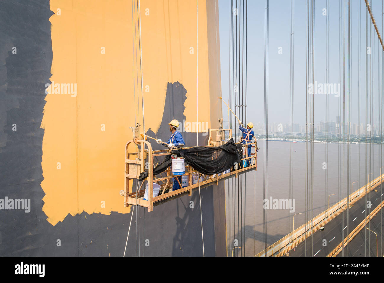 Chinese workers labor at the construction site, coating the pillars of the Yangsigang Bridge, the World's longest double-deck suspension bridge, acros Stock Photo