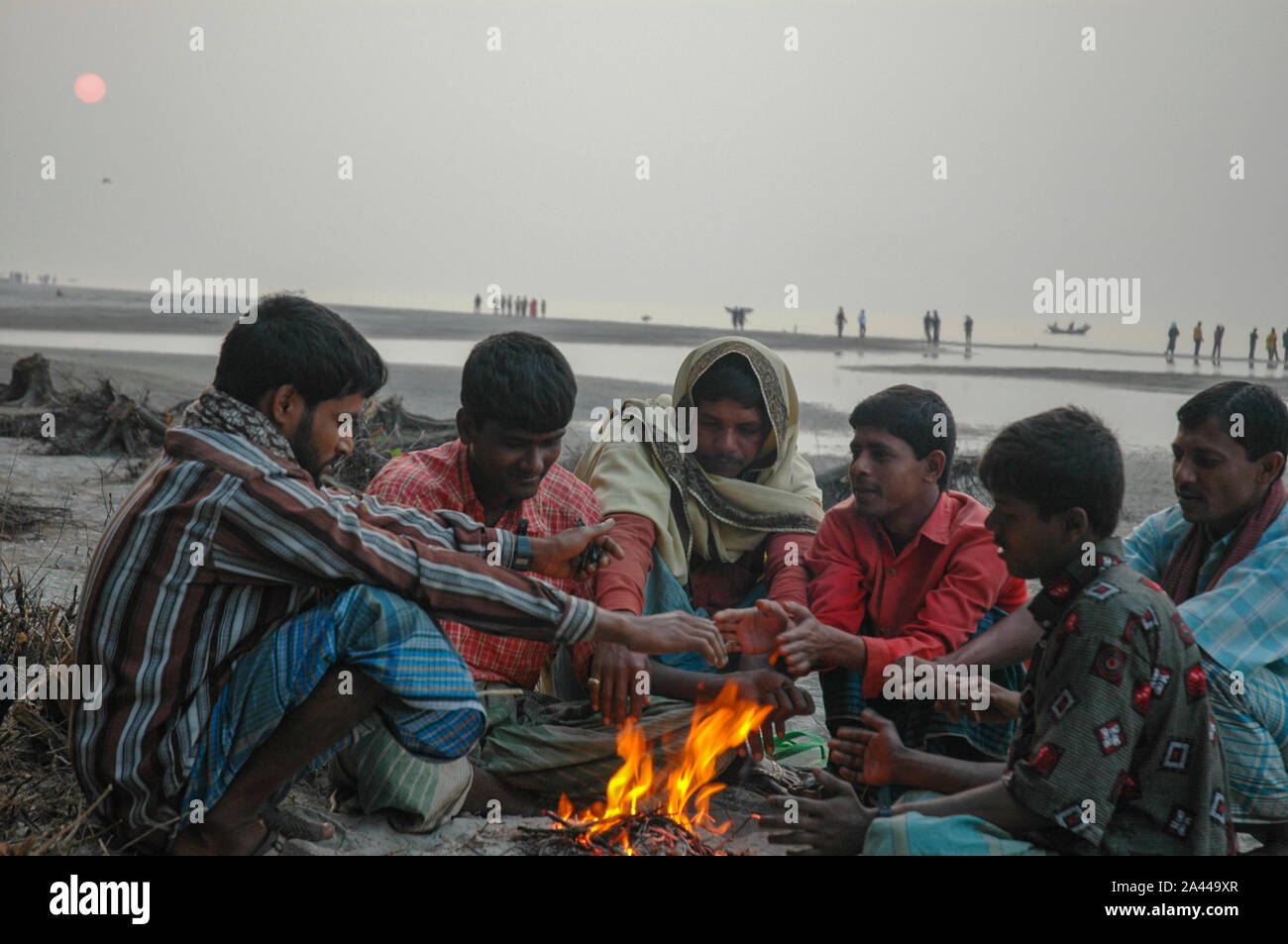 Low-income people warm themselves in the heat from burning wastes in a winter morning at Kuakata sea beach. Patuakhali, Bangladesh. Stock Photo