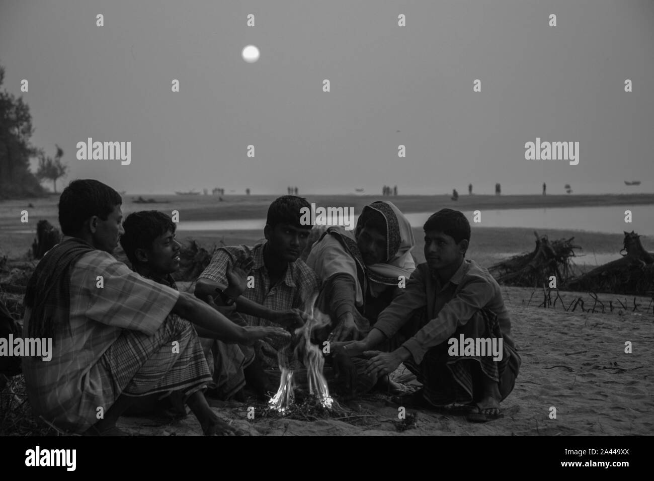 Low-income people warm themselves in the heat from burning wastes in a winter morning at Kuakata sea beach. Patuakhali, Bangladesh. Stock Photo