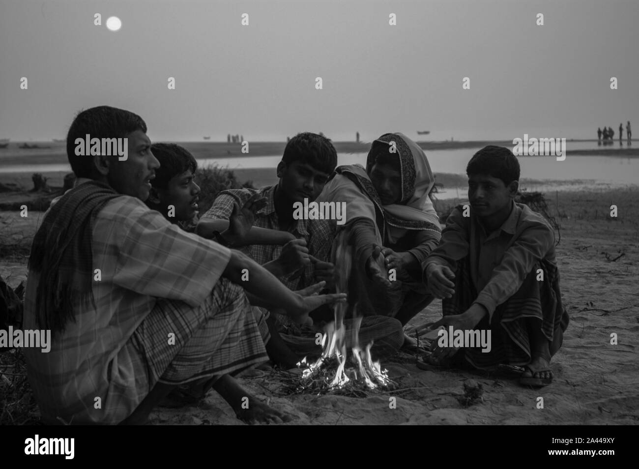 Low-income people warm themselves in the heat from burning wastes in a winter morning at Kuakata sea beach. Patuakhali, Bangladesh. Stock Photo