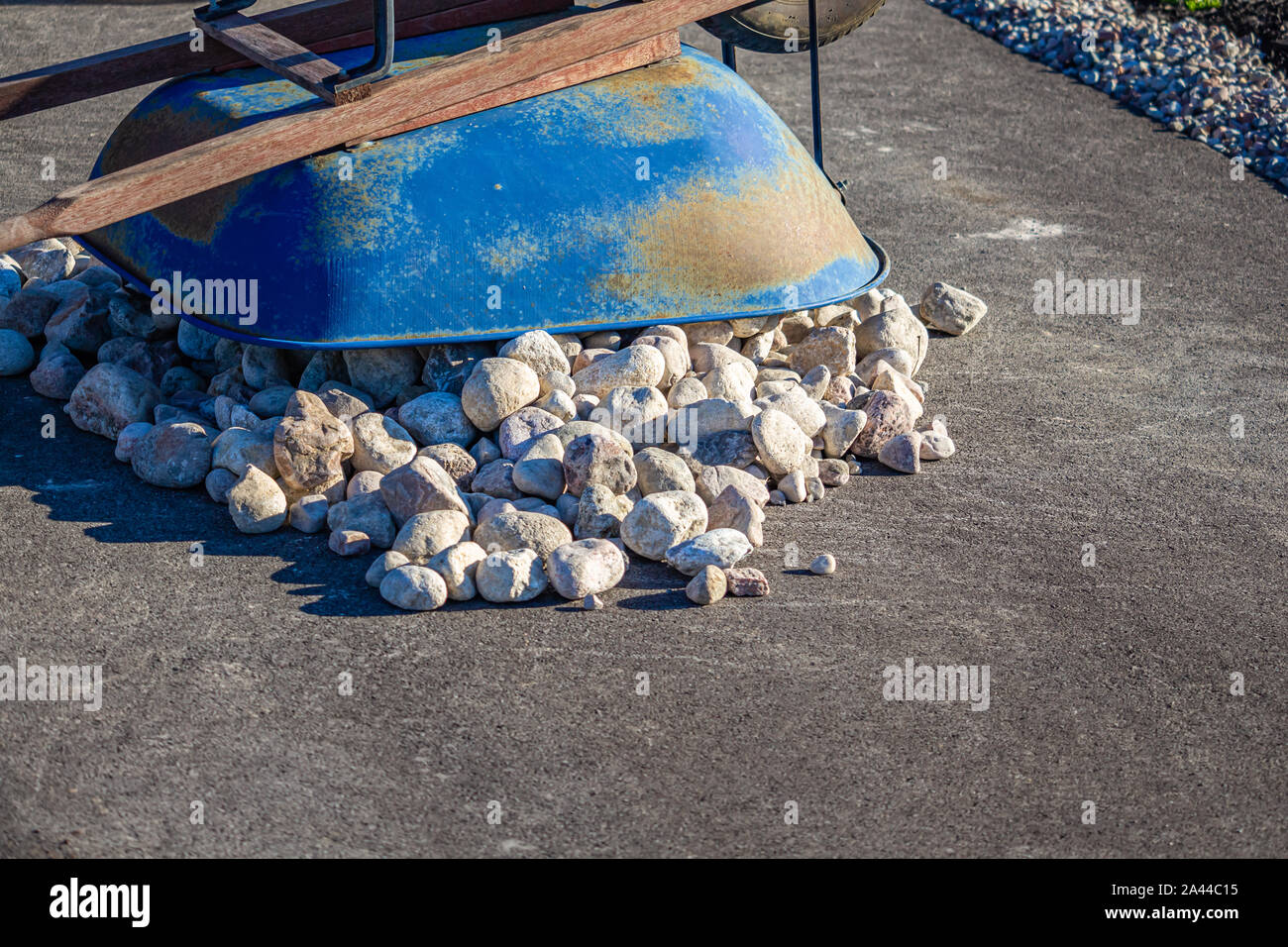 An overturned blue wheelbarrow lies on top of its payload of white stones on an asphalt suburban driveway. Stock Photo