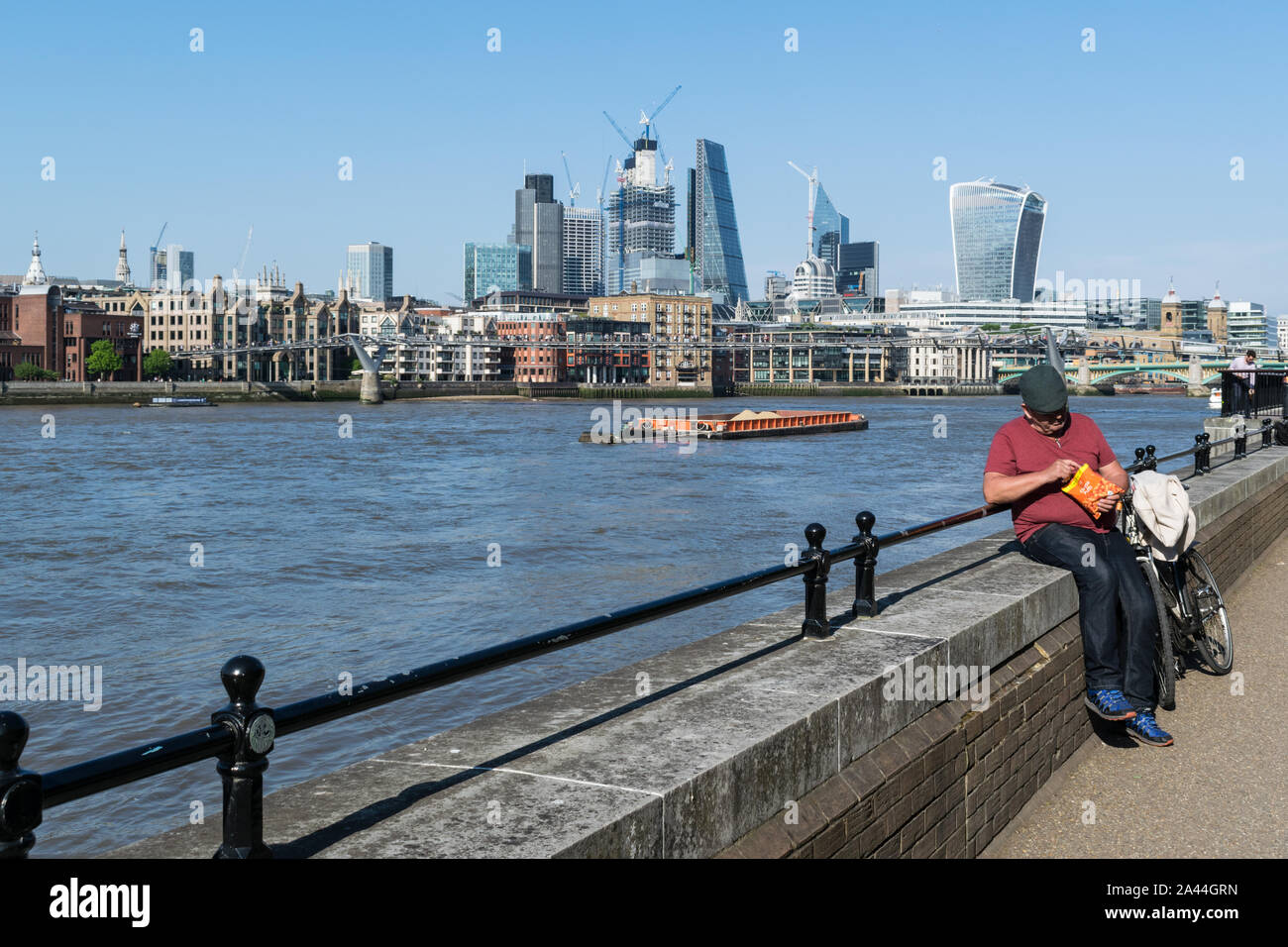 London, England - May 15, 2018:  A man takes a break along the edge of the Thames river on a bright sunny day Stock Photo