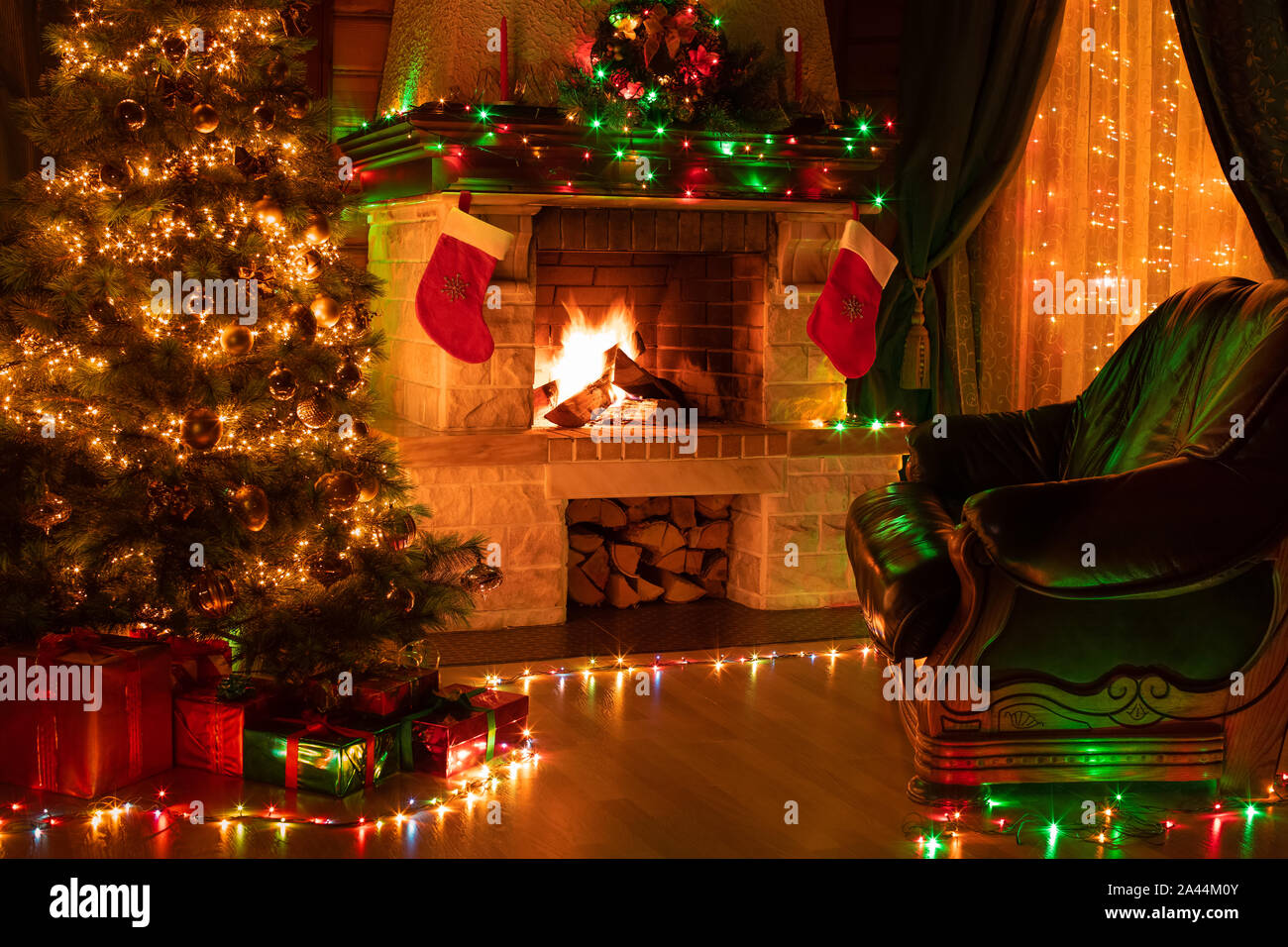 Christmas decorated dark living room interior with fireplace, armchair, window and xmas tree Stock Photo