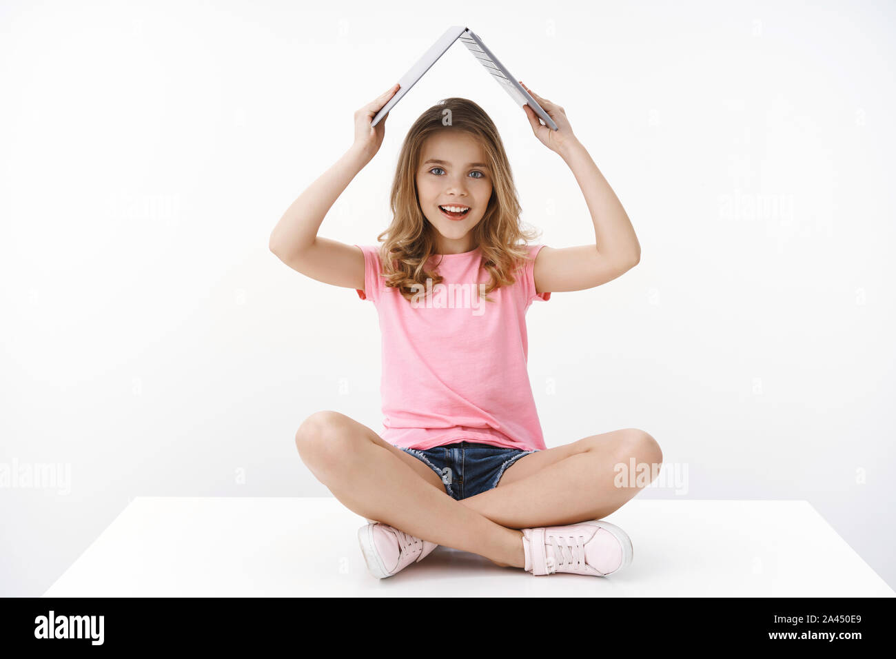Smart cute blond caucasian little cheerful girl child sitting on floor amused excited, raise laptop under head like roof, smiling broadly, like studyi Stock Photo