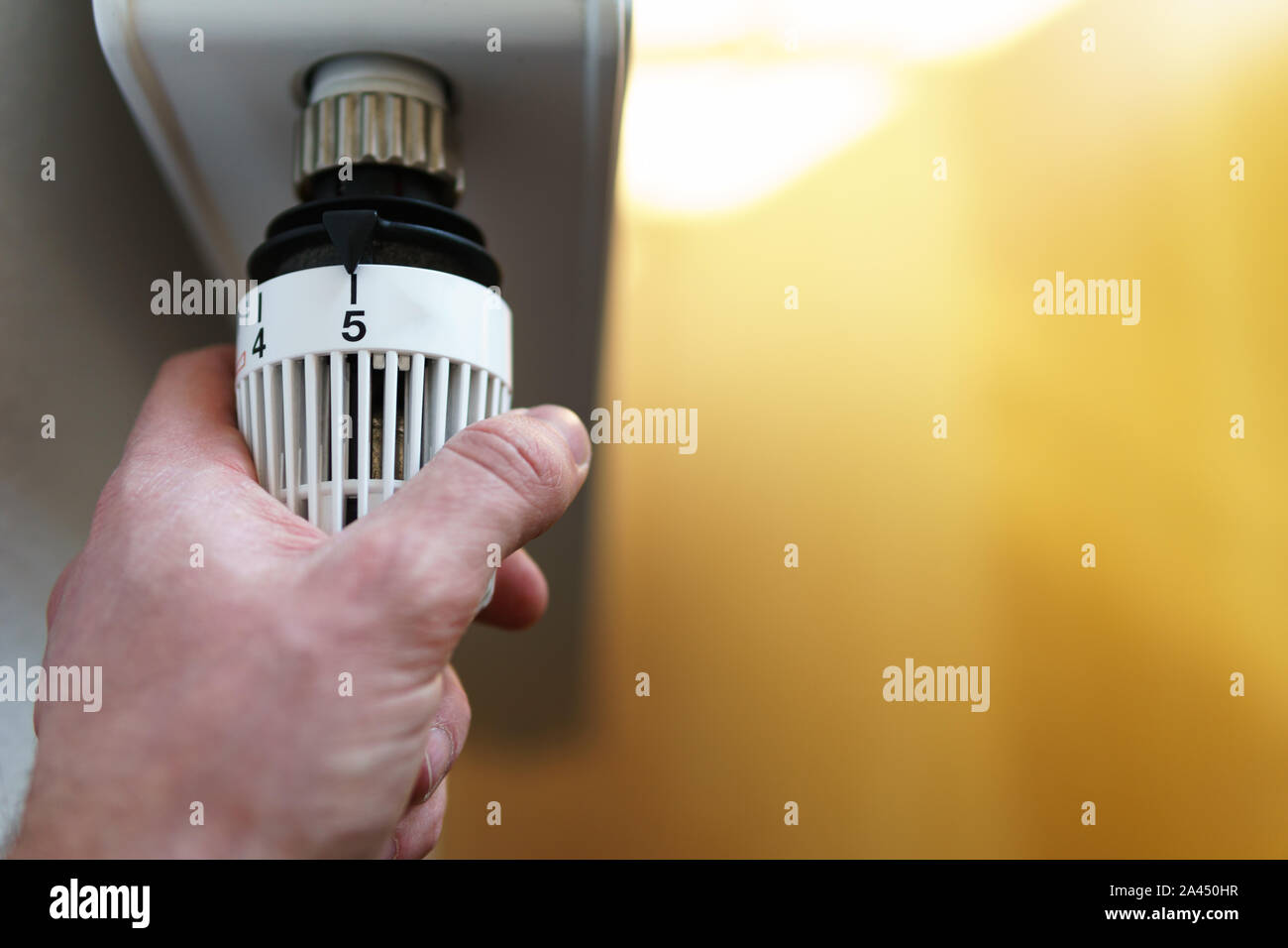 Hand of man adjusting radiator thermostat valve up to number five icon, symbol for high heating costs or warm (high) temperature setting, closeup, hor Stock Photo