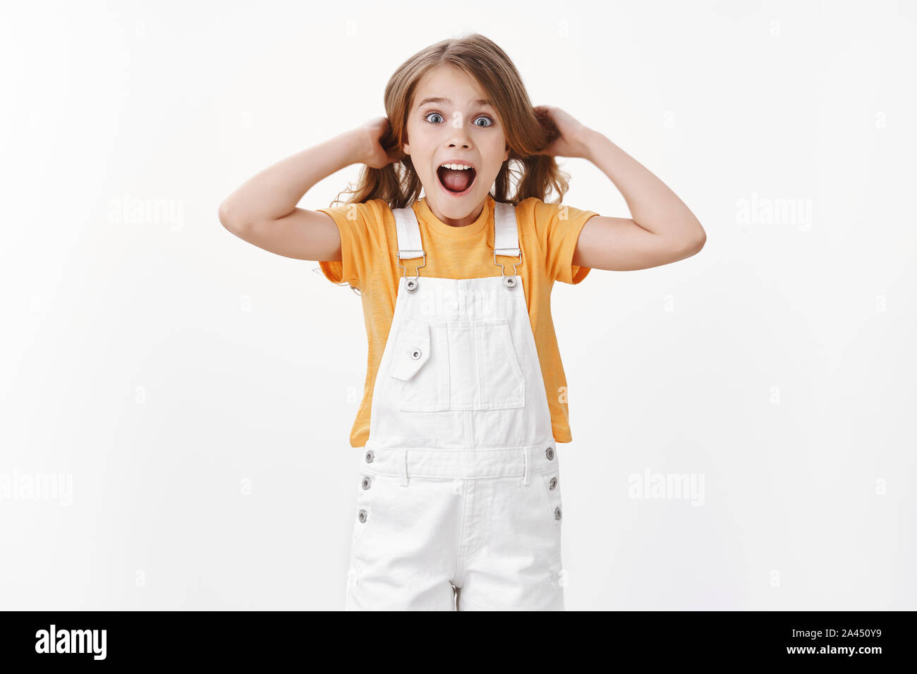 Happy excited child having fun, standing playful and surprised, girl touching hair lifting haircut in air, shouting amused and joyful, express enthusi Stock Photo