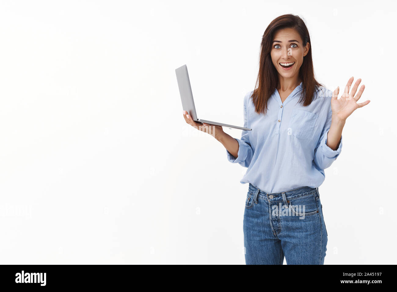 Happy relieved good-looking brunette female office worker sighing pleased, finish work writing project in time, waving camera say hi hello, smiling ho Stock Photo