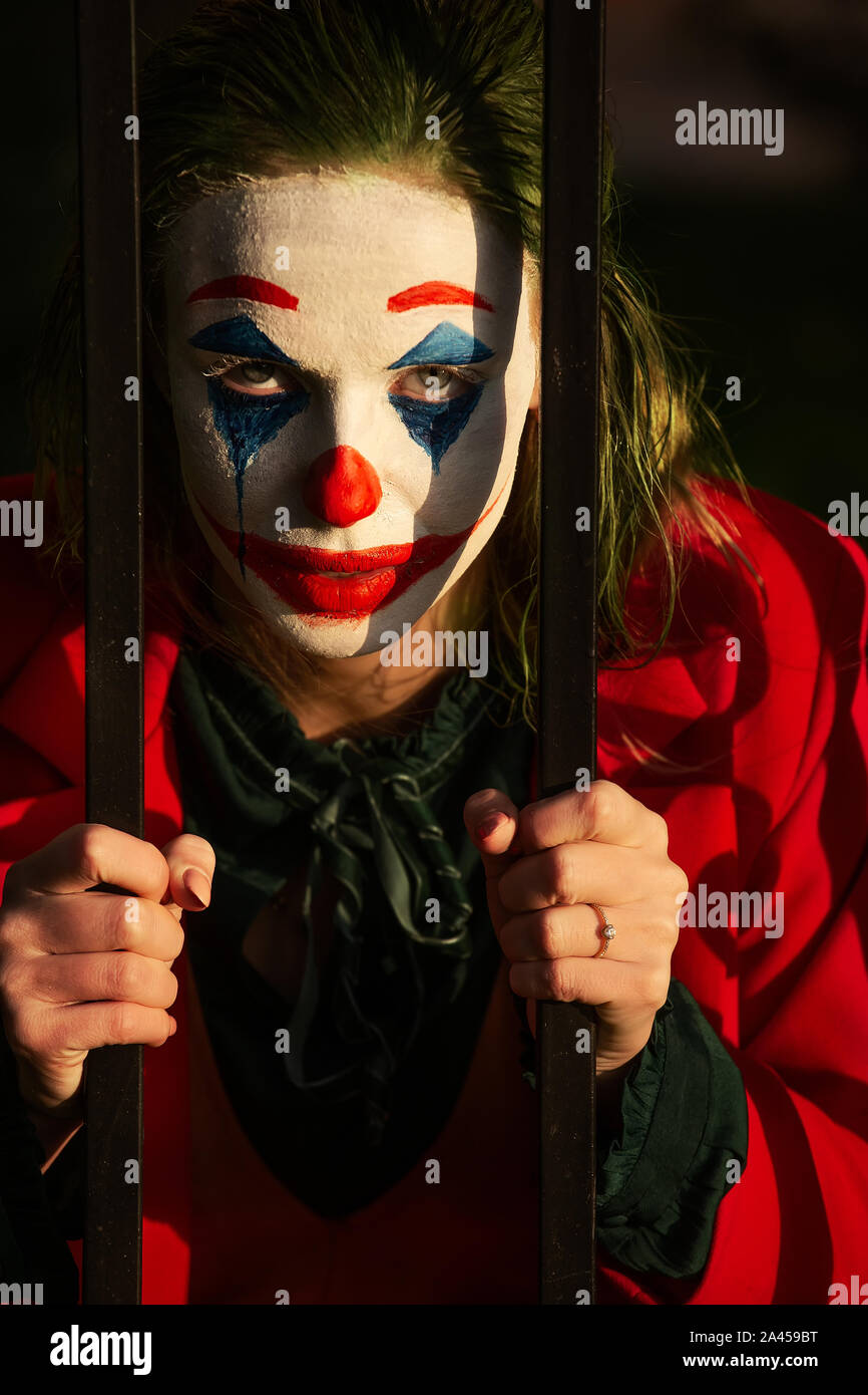 young woman with Joker makeup and costume looking at camera through bars Stock Photo