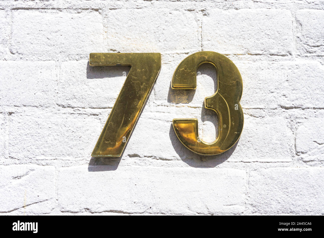 Golde colored house number seventy three (73) on a white painted brick ...