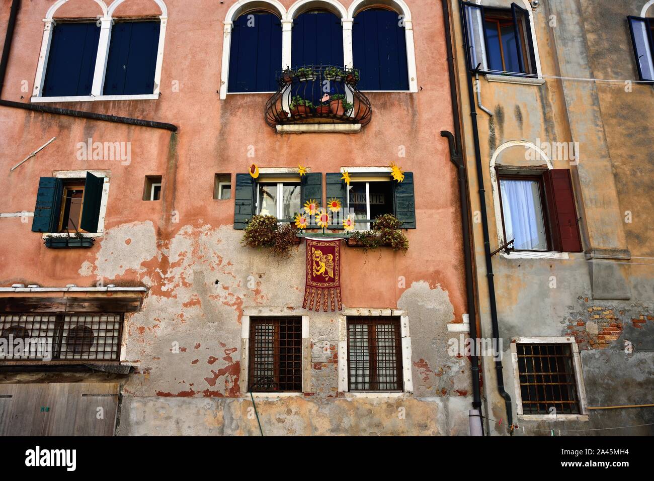 Venice, Italy. A window adorned with flowers and with the flag of San Marco in Sestriere Cannaregio. Stock Photo