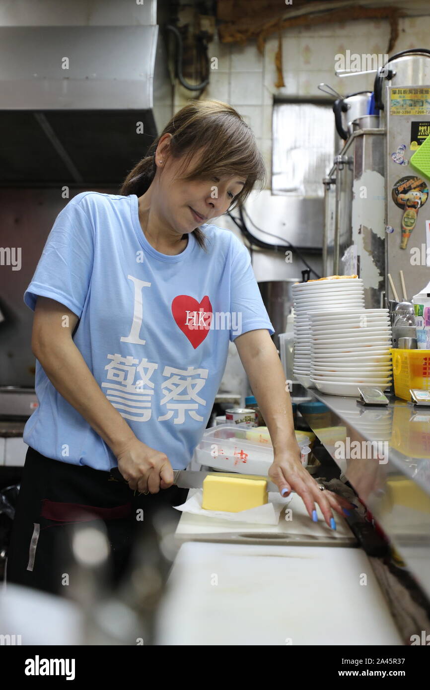 (191012) -- HONG KONG, Oct. 12, 2019 (Xinhua) -- Kate Lee, wearing a T-shirt with the 'I love HK police' slogan on it, prepares food at her tea restaurant in Kowloon, south China's Hong Kong, Oct. 11, 2019. Nestling in the labyrinthine seafood market of the quiet Lei Yue Mun fishing village in Hong Kong, a snug little tea restaurant has unexpectedly become a beacon of courage for ordinary Hong Kong people seeking peace amid the recent chaos. After she posted pictures backing up Hong Kong police against some radical protesters at the end of June, Kate Lee, the owner of the tea restaurant, Stock Photo