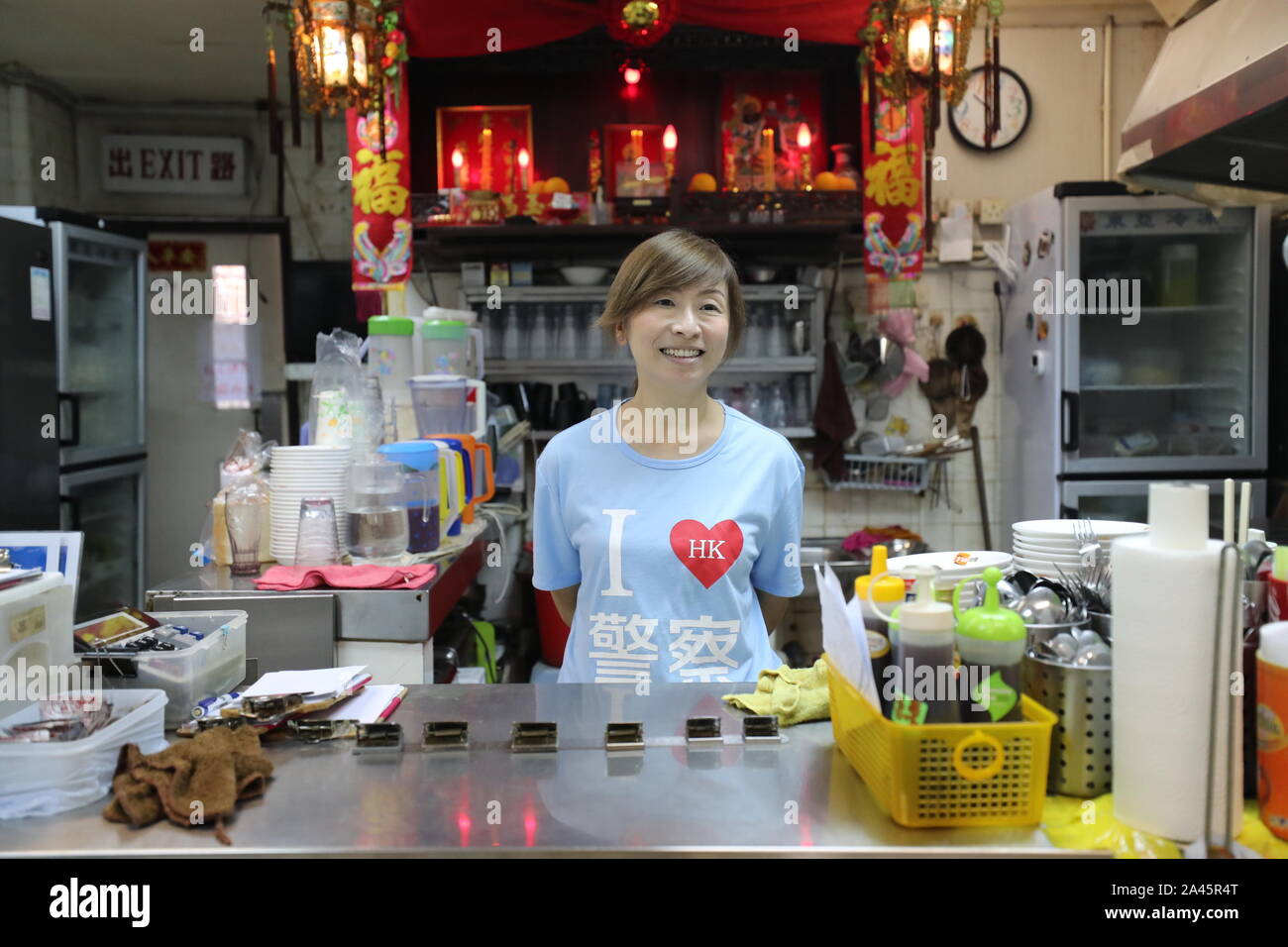 (191012) -- HONG KONG, Oct. 12, 2019 (Xinhua) -- Kate Lee, wearing a T-shirt with the 'I love HK police' slogan on it, waits for customers at her tea restaurant in Kowloon, south China's Hong Kong, Oct. 10, 2019. Nestling in the labyrinthine seafood market of the quiet Lei Yue Mun fishing village in Hong Kong, a snug little tea restaurant has unexpectedly become a beacon of courage for ordinary Hong Kong people seeking peace amid the recent chaos. After she posted pictures backing up Hong Kong police against some radical protesters at the end of June, Kate Lee, the owner of the tea restau Stock Photo