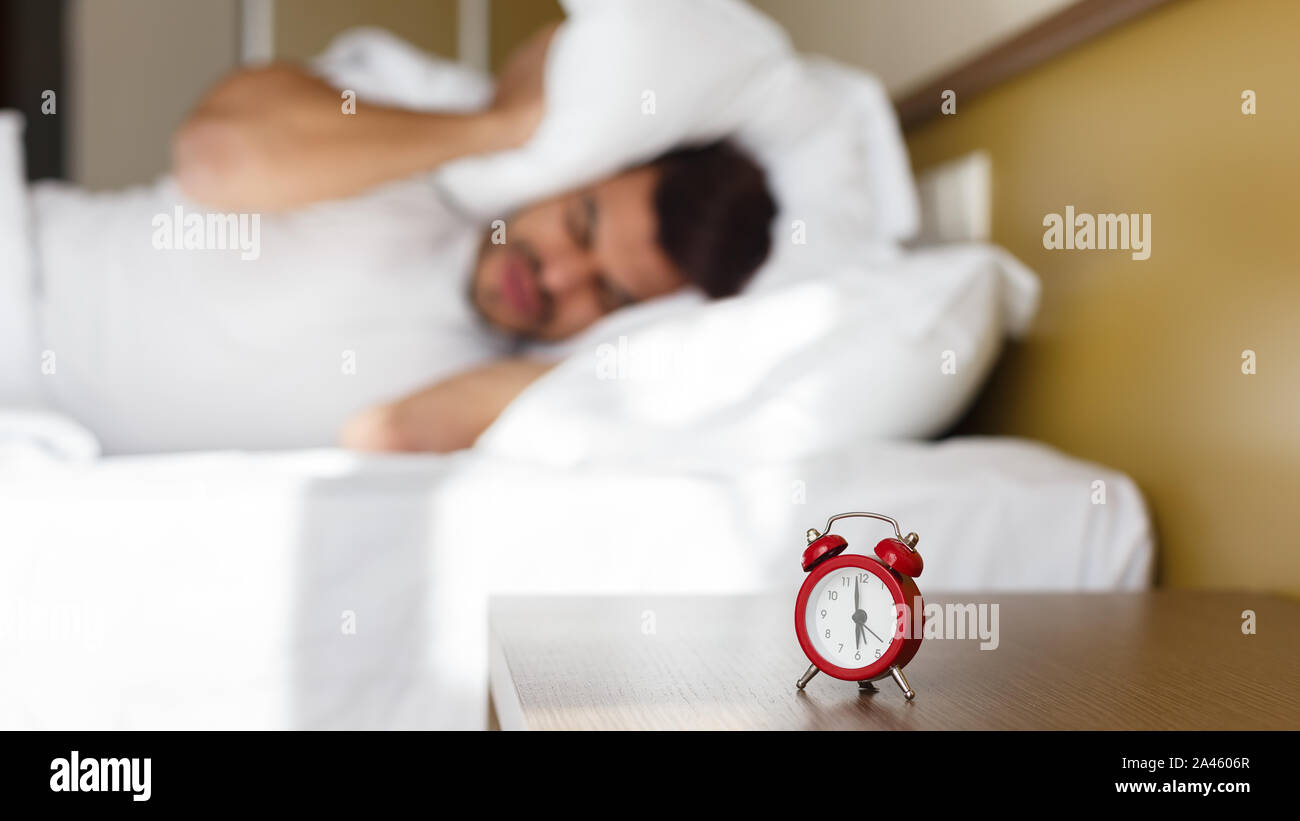 Exhausted man being awaken by alarm clock in his bedroom Stock Photo