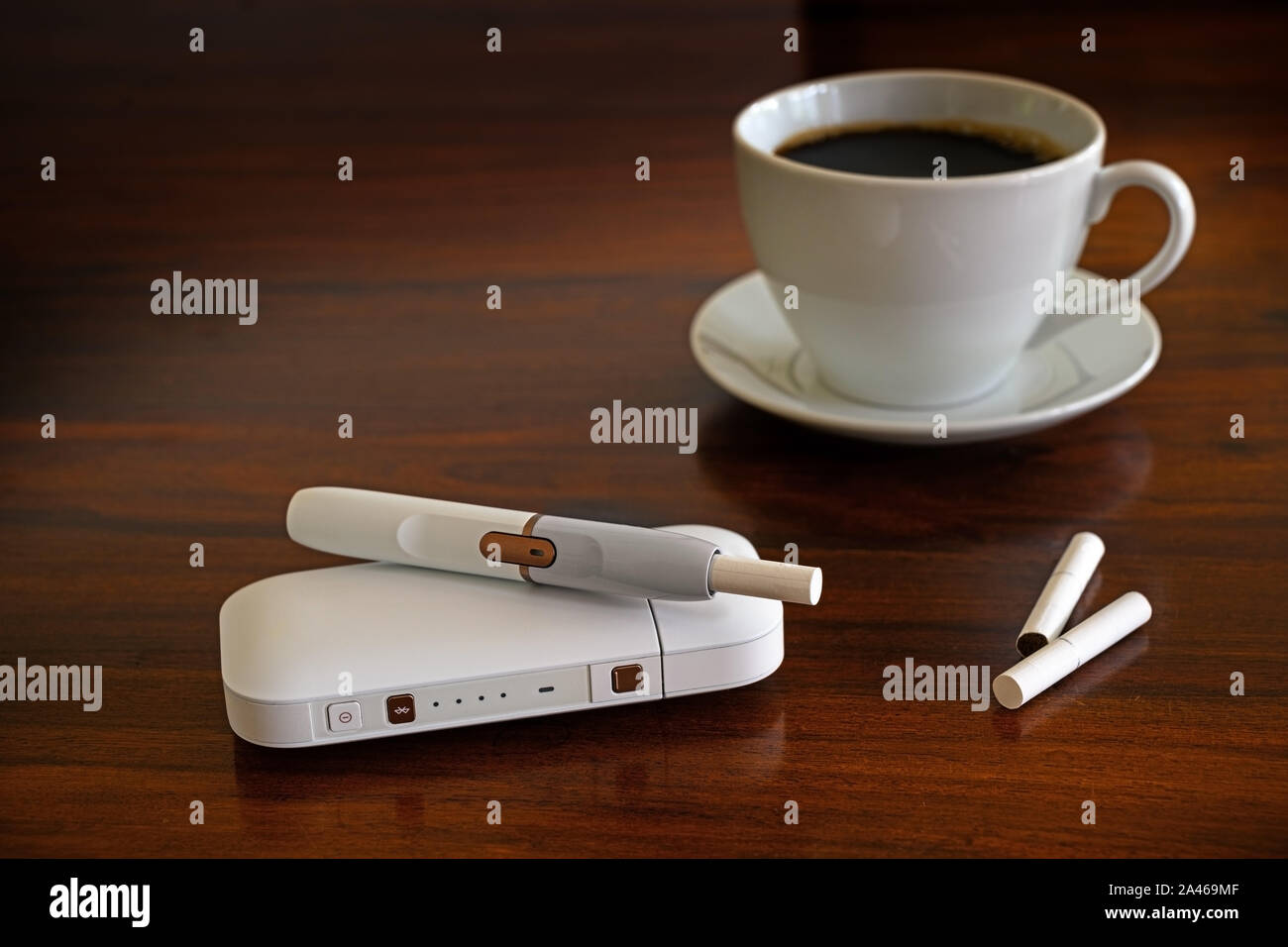 Heating tobacco system and a cup of coffee on a brown table, e-cigarette with tobacco sticks that generates a nicotine aerosol with allegedly fewer to Stock Photo