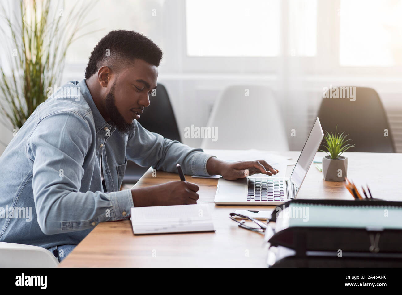 Employee using laptop and taking notes while working in office Stock Photo