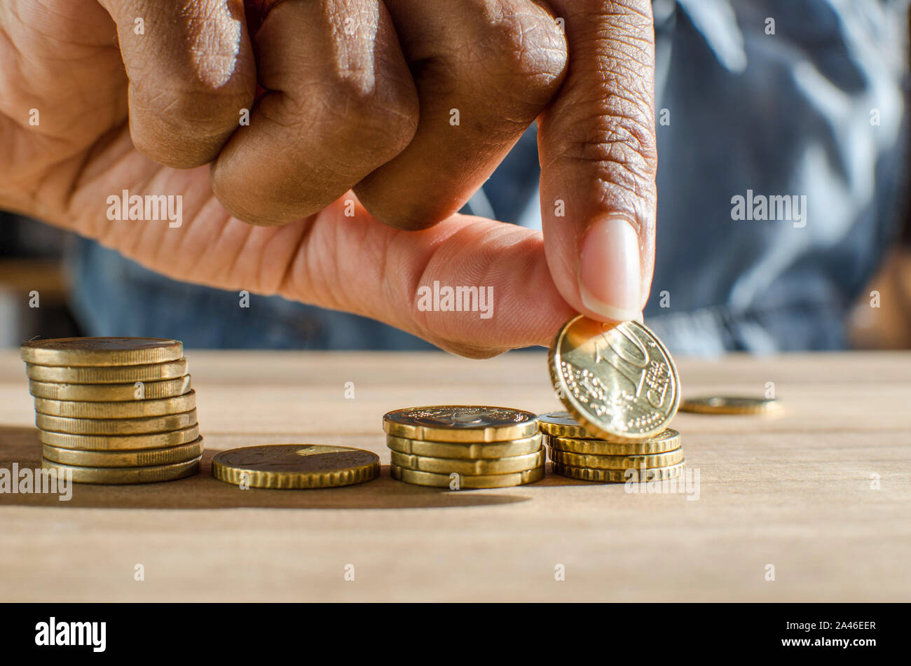 Closeup of a black woman hand counting Euro coins on a wooden table. Selective focus, Stock Photo