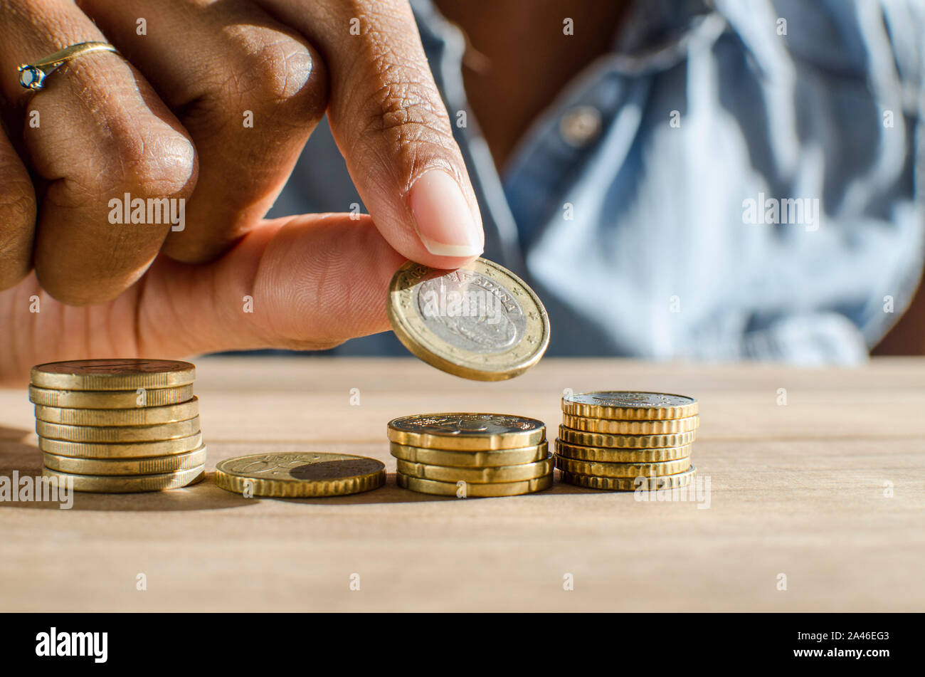 Closeup of a black woman hand counting Euro coins on a wooden table. Selective focus, Stock Photo