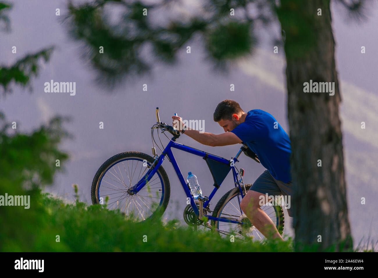 Tired cyclist is wiping his sweat off his face while pushing his ...