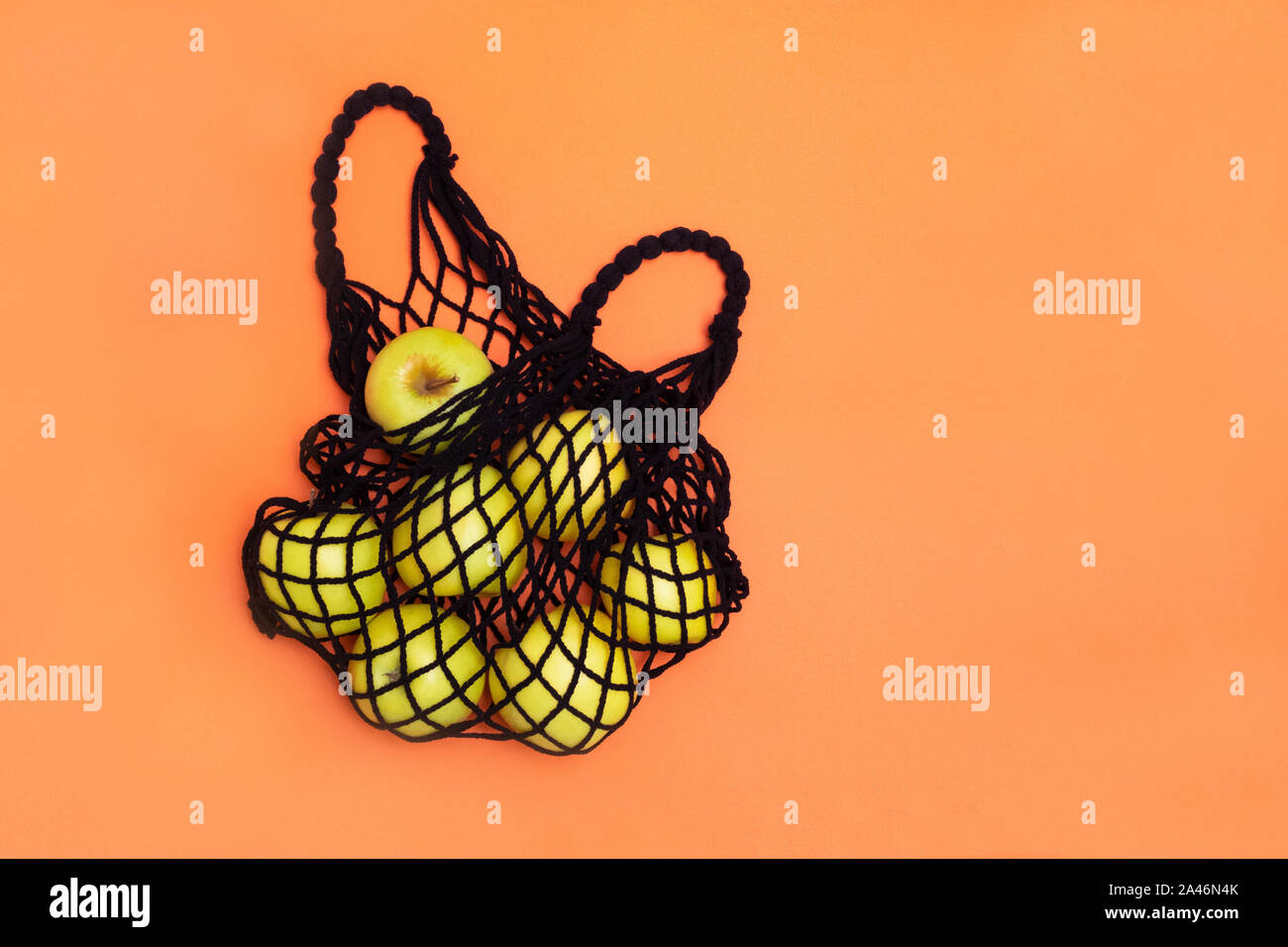 Reusable mesh shopping bag with green apples on orange background. Top