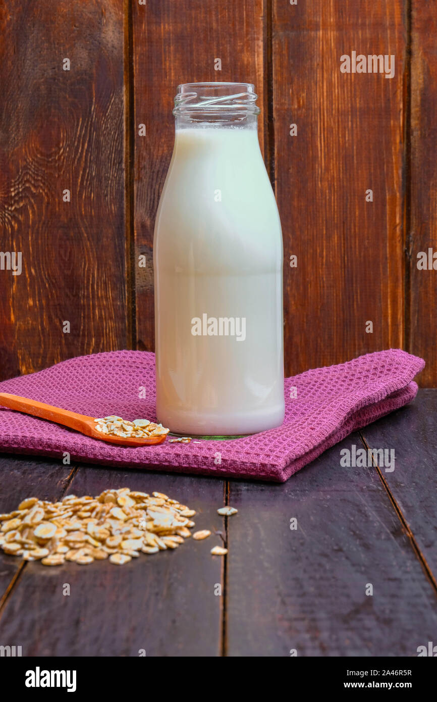 Non-dairy oat milk in a bottle with oat flakes on wooden background Stock Photo