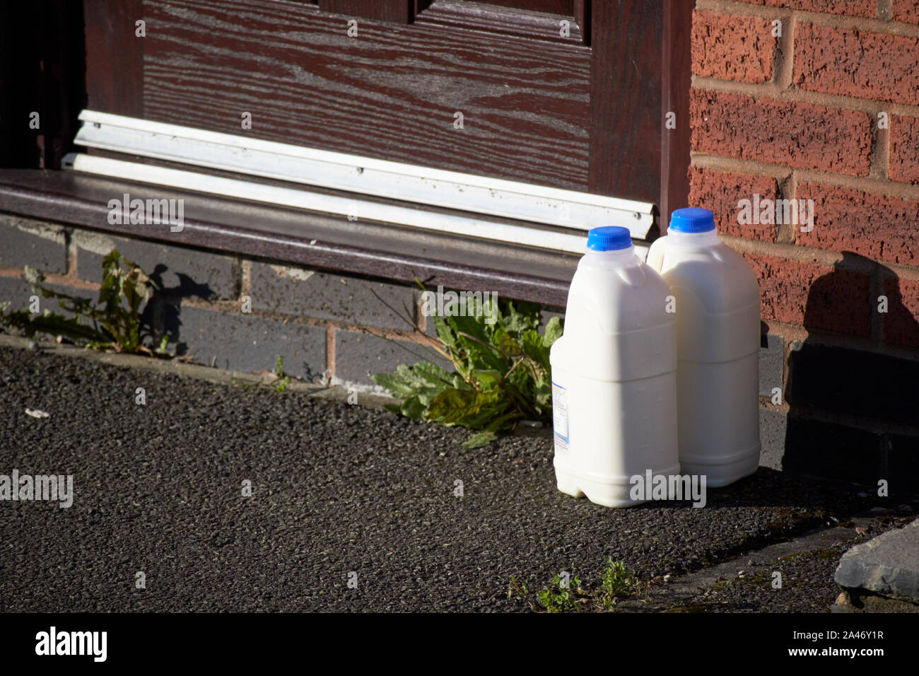 2 plastic containers of milk outside a house doorstep from local milk delivery England UK Stock Photo