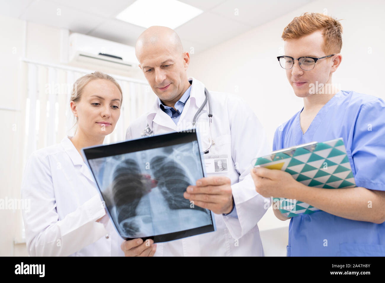 Two doctors discussing x-ray of lungs while young intern making notes Stock Photo