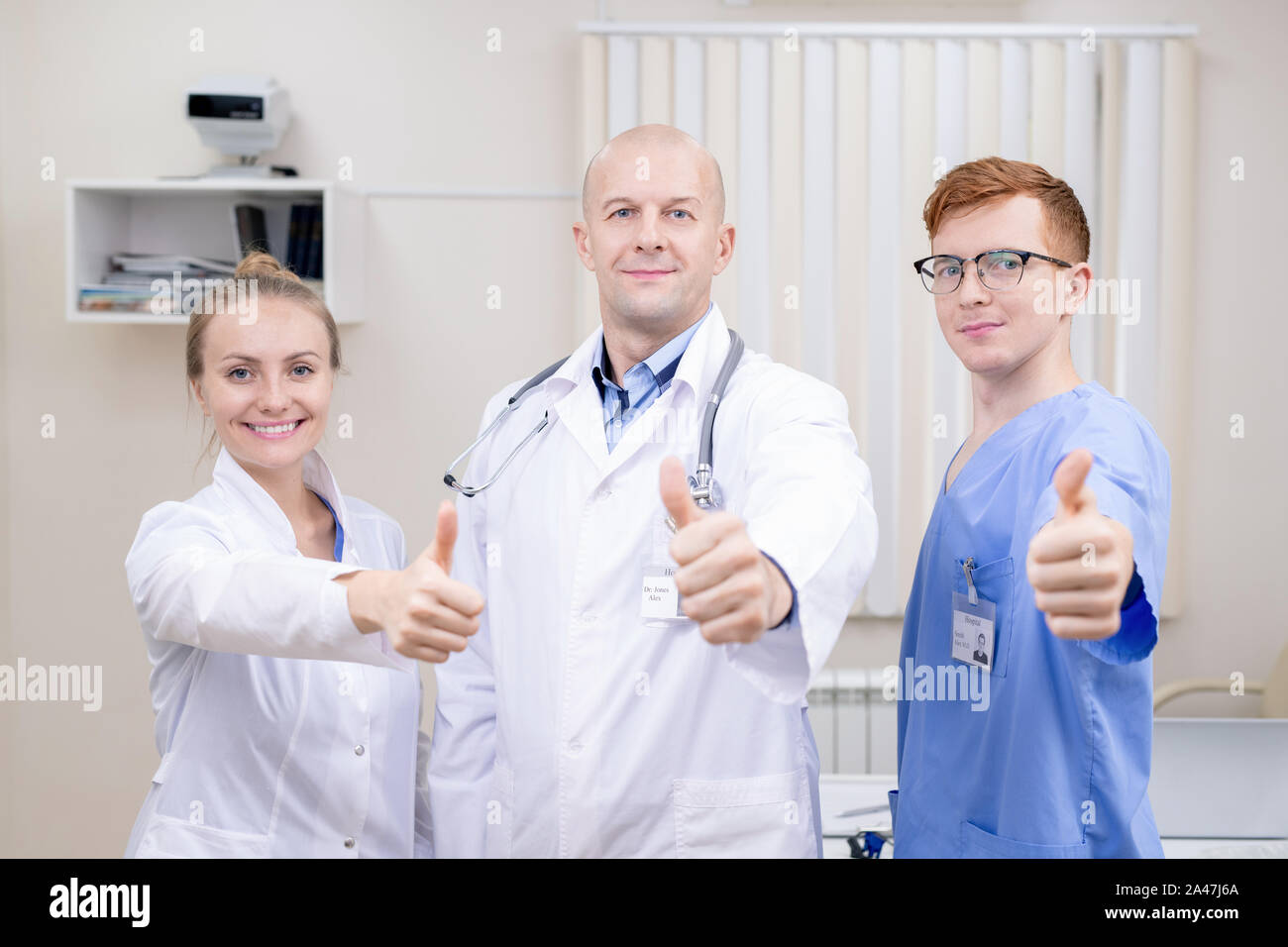 Three successful professionals in medical uniform showing thumbs up Stock Photo