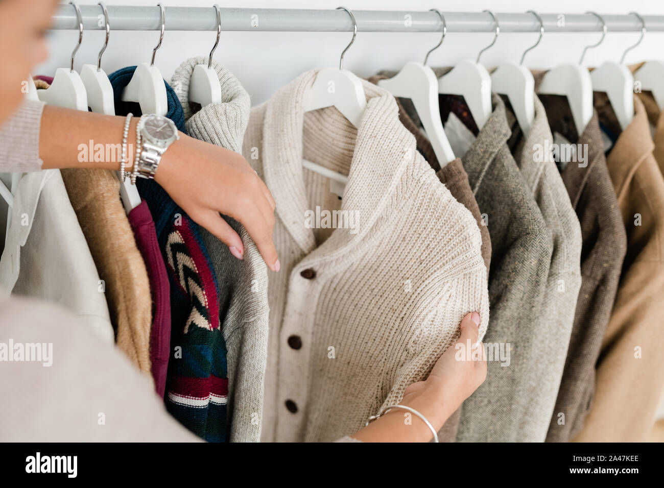 Hands of young woman holding white knitted cardigan while choosing new clothes Stock Photo