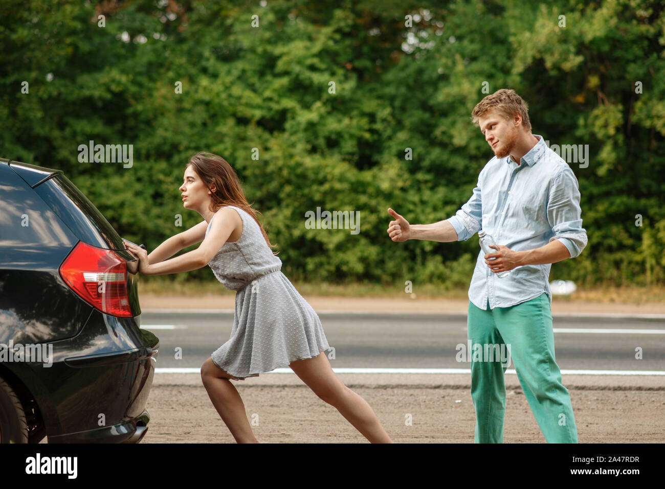 Young couple pushing broken car on road, breakdown Stock Photo