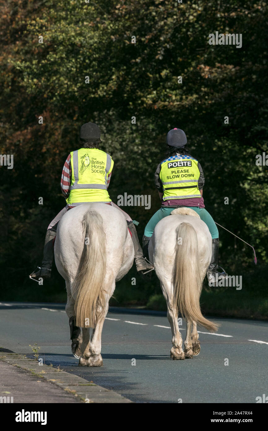 A pair of female horse riders with yellow hi viz jackets on riding on road near Preston in lancashire Stock Photo