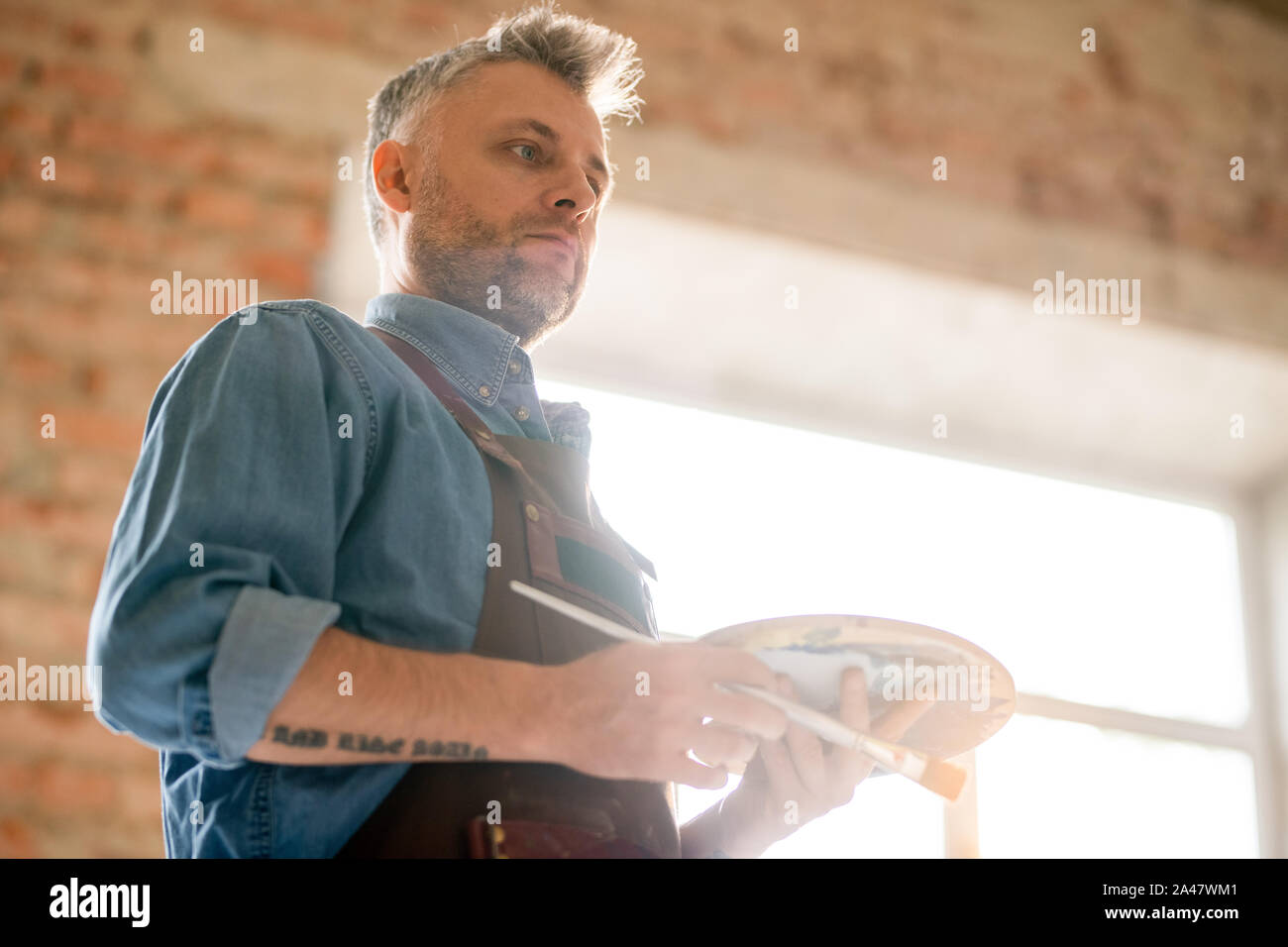 Pensive or serious middle aged man in workwear thinking of ideas at work Stock Photo